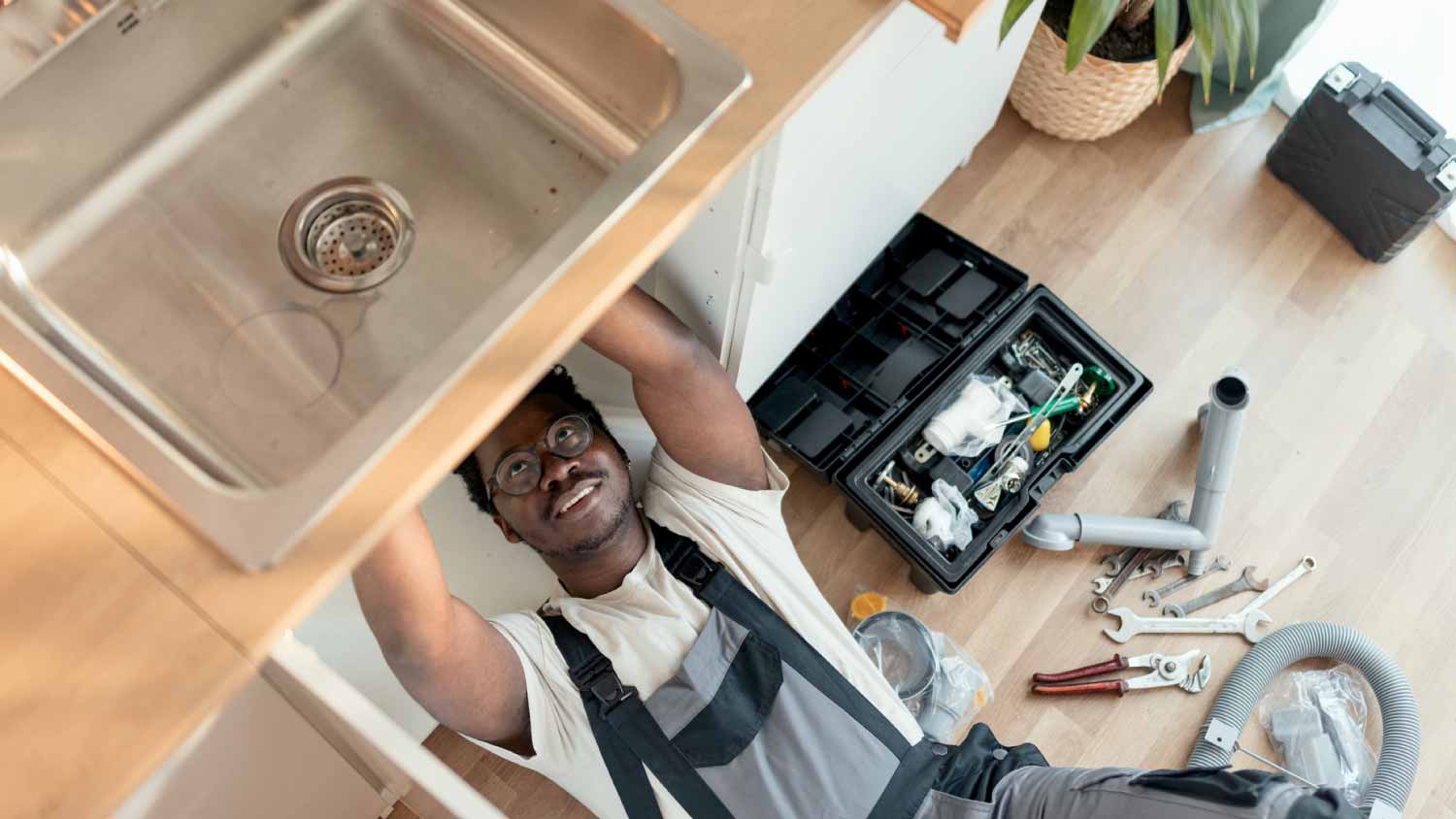 A plumber working diligently under a sink, showcasing the importance of immediate actions during plumbing emergencies.